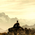 Mann sitzt an einer Klippe und schaut in die Berge