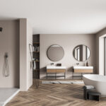 Beigefarbenes Panorama-Badezimmer mit Duschkabine, trendigen, runden Spiegeln mit zwei Waschtischen, einer ovalen, weißen Keramikbadewanne und Parkettboden.